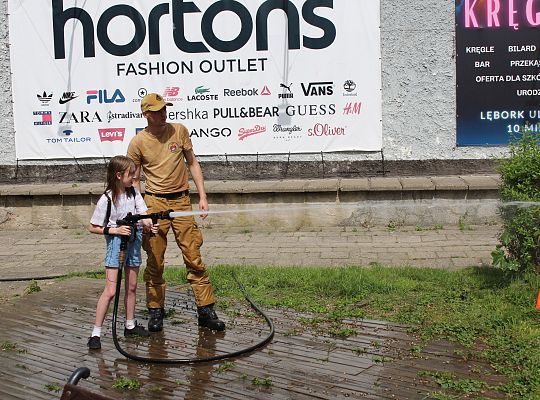 Grafika 17. Strażak OSP z dziewcznką leją wodę z węża strażackiego