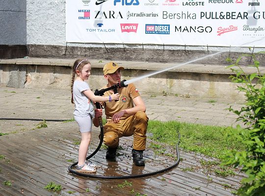 Grafika 18. Strażak OSP z dziewcznką leją wodę z węża strażackiego